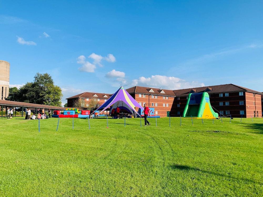 A beautiful day with a blue sky and vibrant green grass. A purple tent and an inflatable slide are set up, creating a fun and lively outdoor atmosphere.